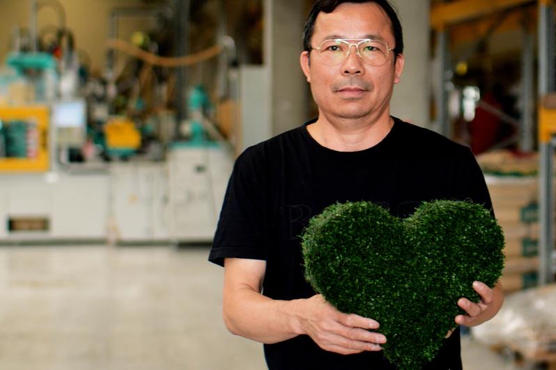 Mann in Produktionshalle mit grünem Herz aus Kunstrasen.