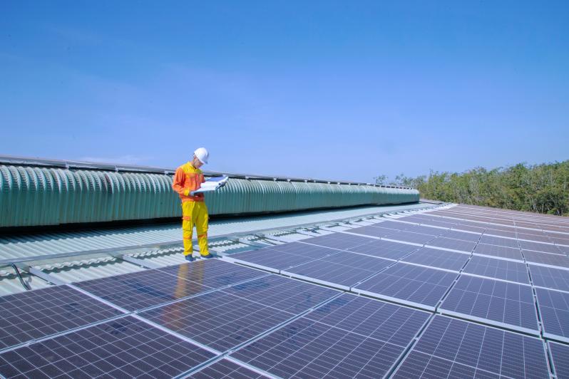 Mann in Arbeitskleidung steht auf großer Photovoltaikfläche, die auf einem Hausdach angebracht ist. 