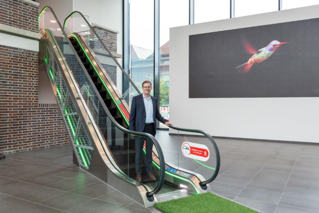 Portrait des Geschäftsleiters Supply Chain der Schindler AG Jörg Naescher auf einer kurzen Rolltreppe in der Eingangshalle eines Bürogebäudes. An deren Fuß wartet ein ausgerollter grüner Teppich aus ökologischem Rollrasen auf ihn.